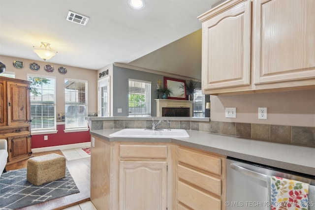 kitchen featuring visible vents, stainless steel dishwasher, a fireplace, a sink, and light brown cabinets