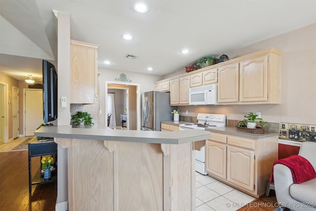 kitchen with a breakfast bar, light brown cabinets, white appliances, a peninsula, and visible vents