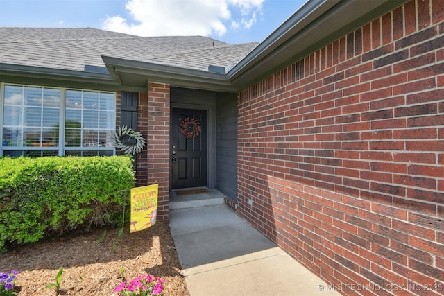 entrance to property featuring brick siding and roof with shingles