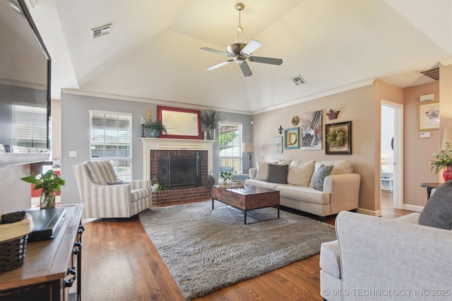 living area with a ceiling fan, visible vents, a fireplace, vaulted ceiling, and wood finished floors