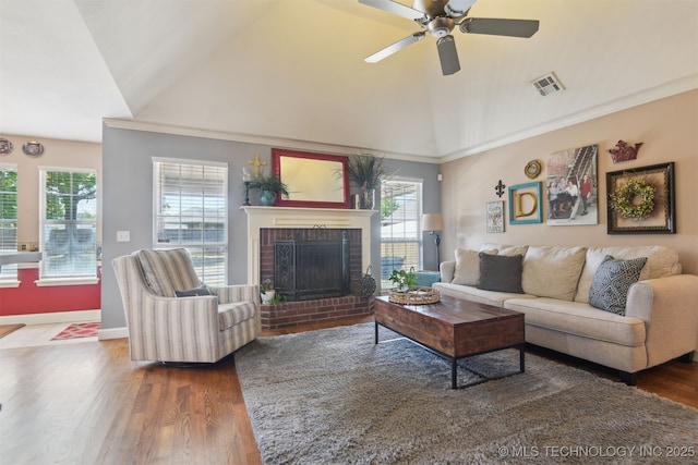 living room with ceiling fan, visible vents, a brick fireplace, wood finished floors, and vaulted ceiling