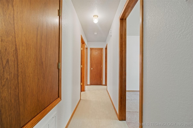 hallway featuring light colored carpet and baseboards