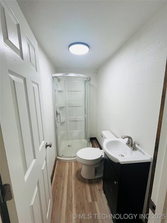 bathroom featuring vanity, wood finished floors, toilet, and a stall shower