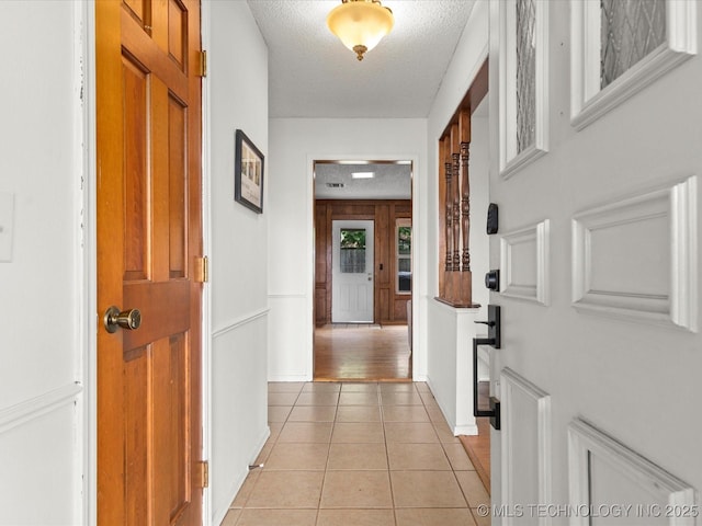 hall with light tile patterned floors, a textured ceiling, and baseboards