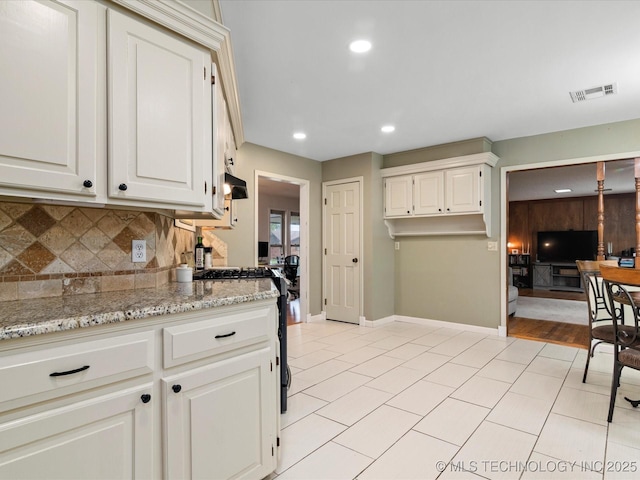 kitchen with decorative backsplash, visible vents, gas range, baseboards, and light stone countertops