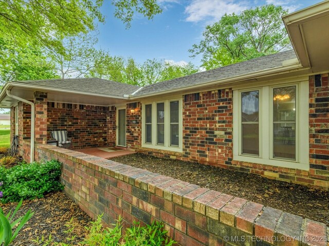 back of house with a shingled roof and brick siding