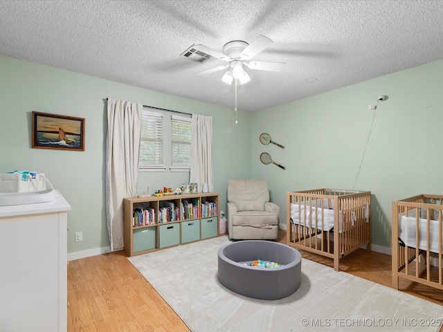 bedroom with wood finished floors, a nursery area, baseboards, visible vents, and a textured ceiling