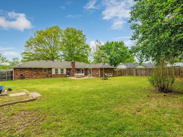 rear view of house with a chimney, a fenced backyard, brick siding, a patio, and a lawn