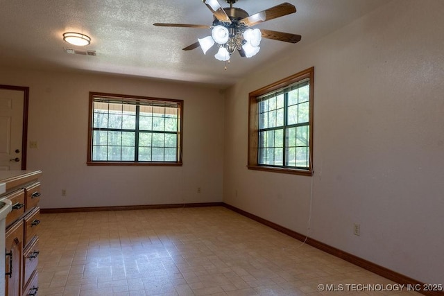empty room with a textured ceiling, visible vents, ceiling fan, and baseboards