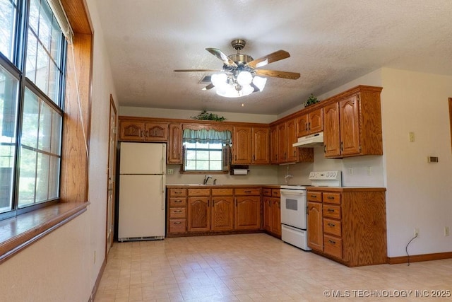 kitchen with white appliances, under cabinet range hood, brown cabinets, a sink, and a textured ceiling