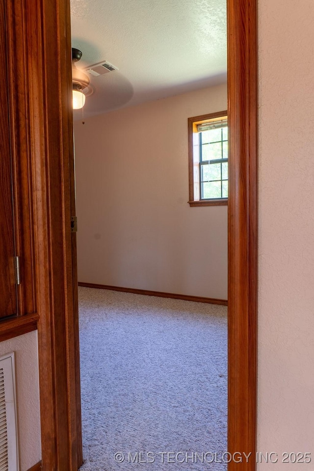 spare room featuring a ceiling fan, visible vents, carpet floors, and a textured ceiling