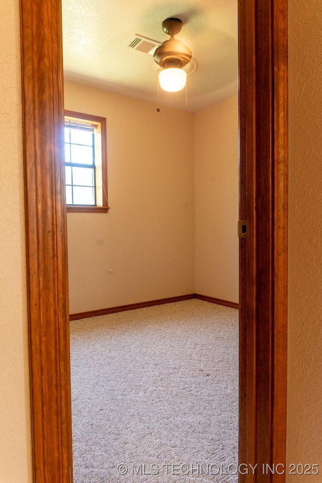 carpeted spare room with baseboards, visible vents, and a textured wall