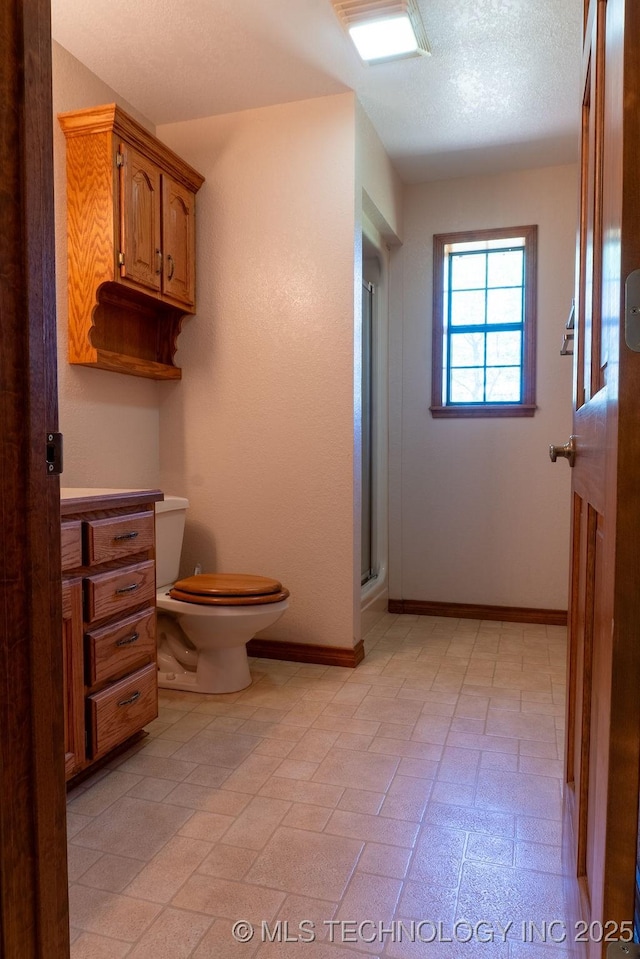 full bathroom with toilet, a shower with shower door, and baseboards