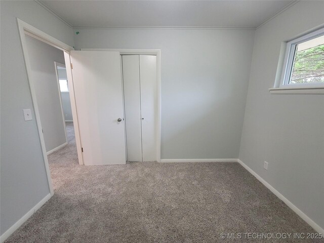 unfurnished bedroom with baseboards, ornamental molding, a closet, and carpet flooring