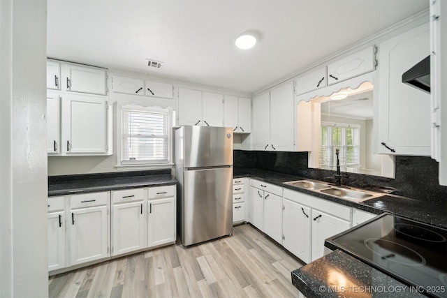 kitchen with dark countertops, white cabinets, freestanding refrigerator, and a sink