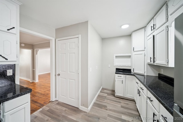 kitchen featuring light wood-style flooring, dark stone countertops, white cabinetry, and baseboards