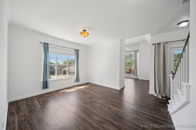 empty room with stairs, baseboards, dark wood-style floors, and a healthy amount of sunlight