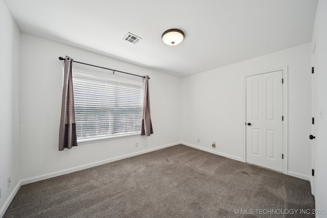 empty room featuring baseboards, visible vents, and dark carpet