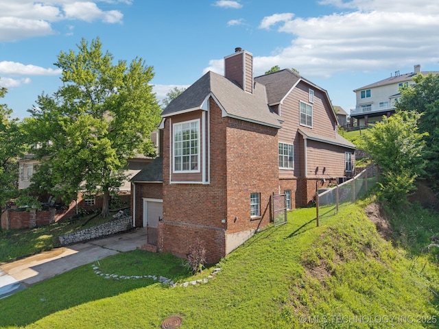 view of side of home with a chimney, a lawn, brick siding, fence, and concrete driveway