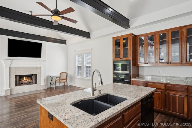 kitchen with dark wood finished floors, a tile fireplace, a sink, black appliances, and glass insert cabinets