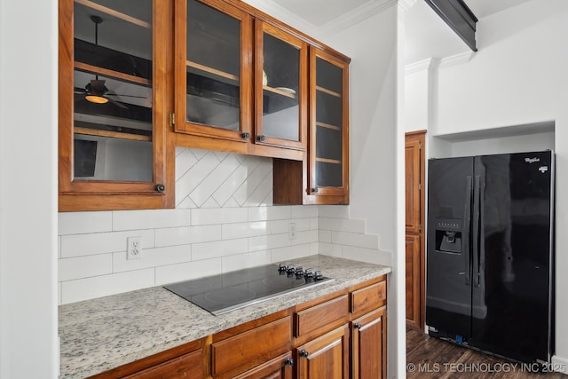 kitchen featuring brown cabinetry, ornamental molding, glass insert cabinets, backsplash, and black appliances