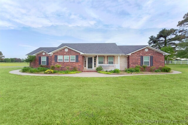 ranch-style home with a shingled roof, covered porch, fence, brick siding, and a front lawn