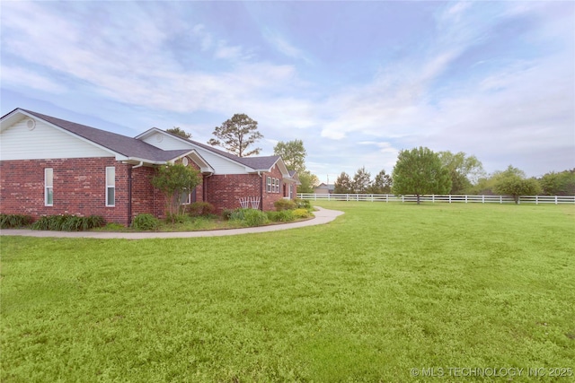 view of side of property with a lawn, fence, and brick siding