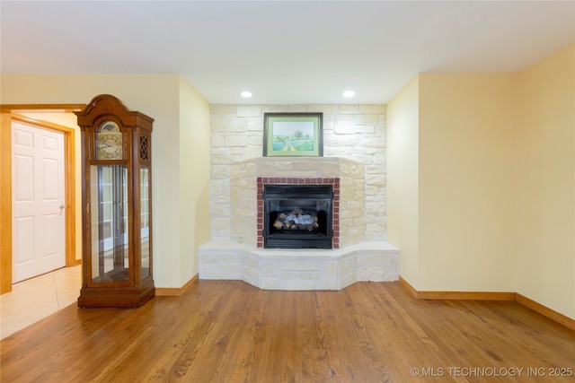 unfurnished living room with baseboards, recessed lighting, wood finished floors, and a stone fireplace