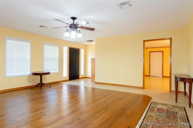unfurnished living room featuring baseboards, visible vents, and a ceiling fan