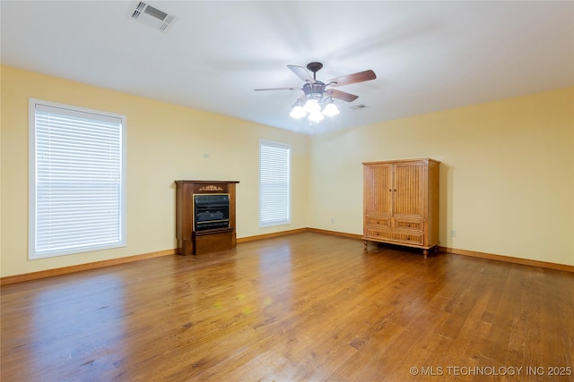 unfurnished living room featuring ceiling fan, a glass covered fireplace, visible vents, and light wood-type flooring