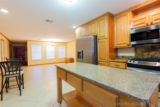 kitchen featuring light stone countertops, stainless steel appliances, light tile patterned flooring, a center island, and visible vents
