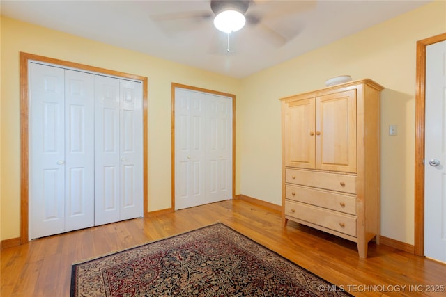 bedroom featuring baseboards, light wood-type flooring, a ceiling fan, and two closets