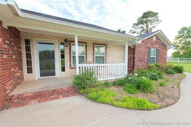 entrance to property with stone siding, a shingled roof, covered porch, and fence
