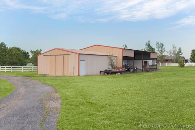 view of pole building with a yard, aphalt driveway, and fence