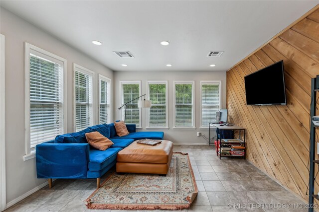 tiled living room featuring visible vents, wood walls, and a healthy amount of sunlight