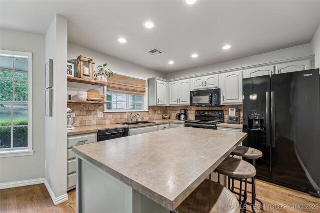 kitchen with a sink, black appliances, visible vents, and tasteful backsplash