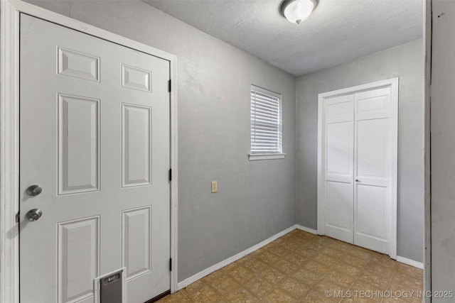 interior space featuring light floors, a textured ceiling, and baseboards