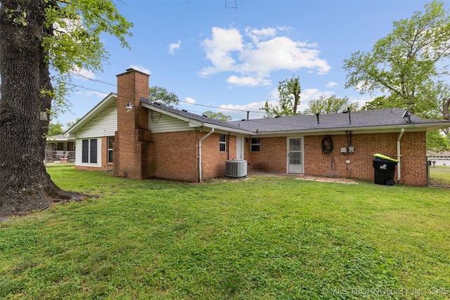 rear view of property with a lawn, a chimney, central AC, and brick siding