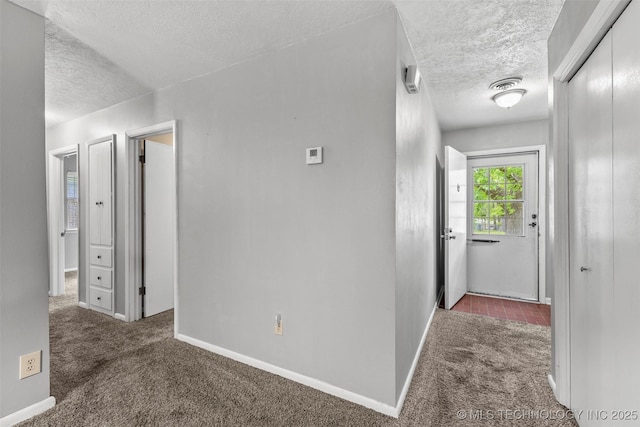 corridor featuring a textured ceiling, carpet floors, and baseboards