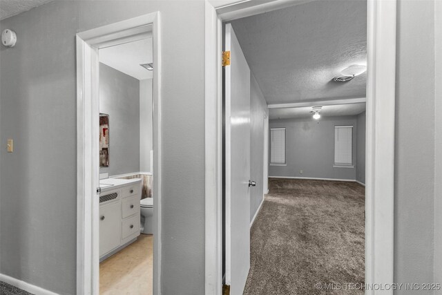 hallway featuring baseboards, a textured ceiling, and light colored carpet