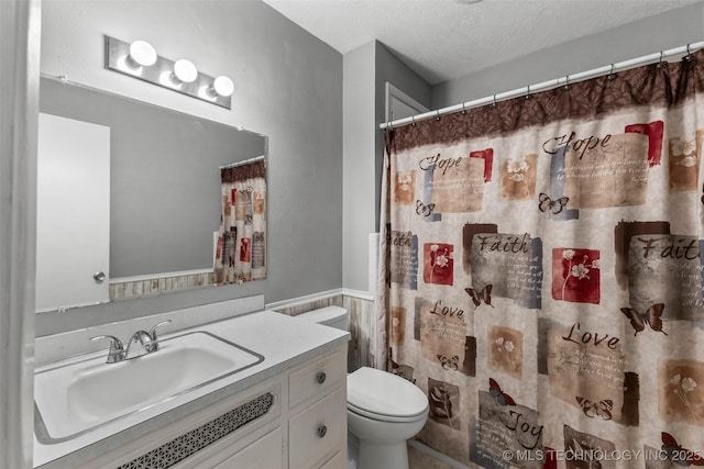 bathroom with tile walls, a wainscoted wall, toilet, vanity, and a textured ceiling