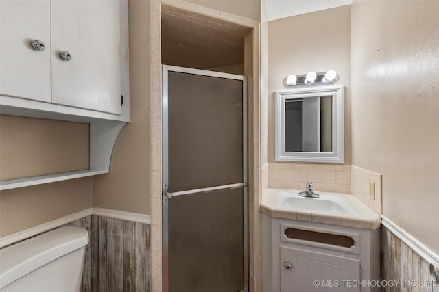 full bath with wainscoting, a shower stall, toilet, and vanity