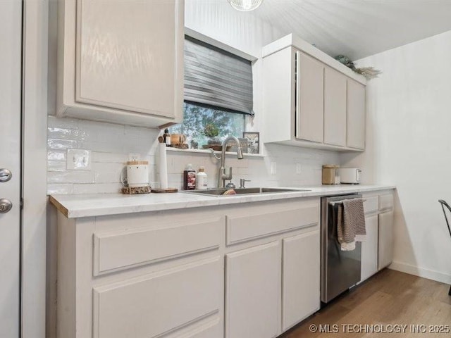 kitchen featuring a sink, backsplash, light countertops, stainless steel dishwasher, and wood finished floors