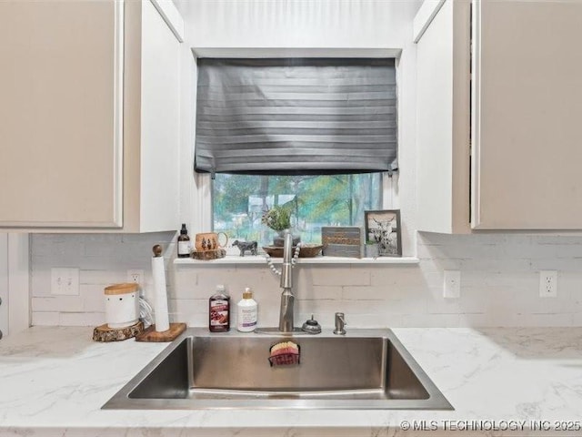 kitchen with light stone countertops, a sink, and backsplash