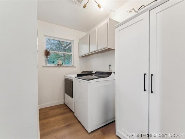 clothes washing area featuring light wood-type flooring, separate washer and dryer, and cabinet space