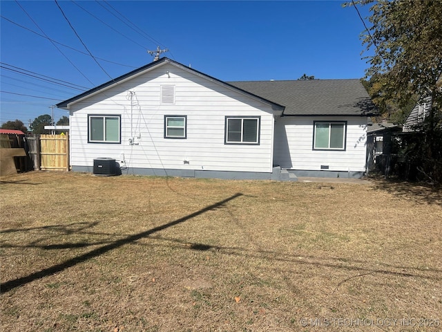 rear view of house with cooling unit, a yard, a shingled roof, and fence