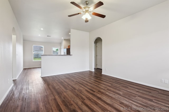 unfurnished living room with recessed lighting, dark wood-style flooring, a ceiling fan, baseboards, and arched walkways