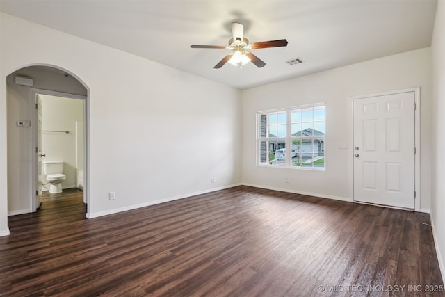 empty room featuring ceiling fan, visible vents, baseboards, arched walkways, and dark wood-style flooring