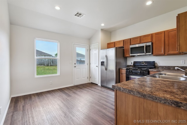 kitchen featuring wood finished floors, stainless steel appliances, dark countertops, a sink, and visible vents
