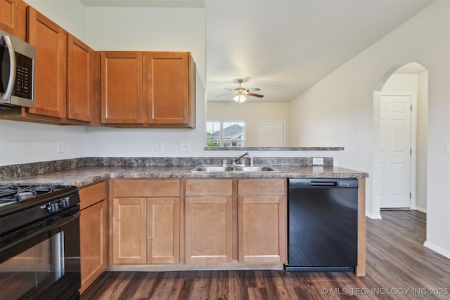 kitchen with a sink, dark wood-style flooring, black appliances, a ceiling fan, and dark countertops